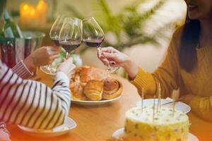 Cheerful friends enjoying home Birthday holiday party. Asian Friends cheering drinking red wine celebrating New Year party. photo