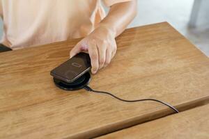 Charging mobile phone battery with wireless charging device in the table. Smartphone charging on a charging pad. Mobile phone near wireless charger Modern lifestyle technology concept. photo