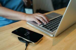 Charging mobile phone battery with wireless charging device in the table. Smartphone charging on a charging pad. Mobile phone near wireless charger Modern lifestyle technology concept photo