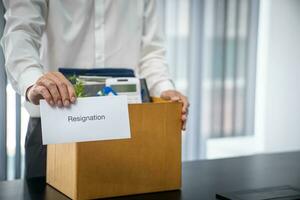 Business man sending resignation letter and packing Stuff Resign Depress or carrying business cardboard box by desk in office. Change of job or fired from company photo