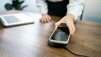 Charging mobile phone battery with wireless charging device in the table. Smartphone charging on a charging pad. Mobile phone near wireless charger Modern lifestyle technology concept. photo