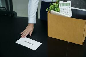 negocio mujer enviando resignación letra a jefe y participación cosas Renunciar deprimir o que lleva cartulina caja por escritorio en oficina foto