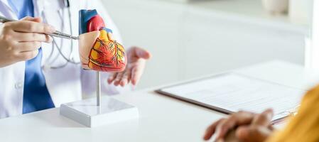 Cardiology Consultation treatment of heart disease. Doctor cardiologist while consultation showing anatomical model of human heart with aged patient talking about heart diseases. photo