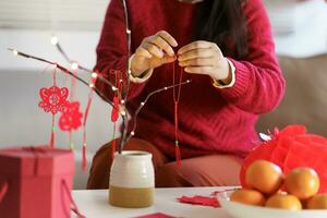 asiático mujer decorado casa para chino nuevo año celebraciones poniendo tradicional colgante a el chino lunar nuevo año para bueno suerte. chino palabra medio bendición foto