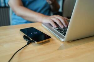 Charging mobile phone battery with wireless charging device in the table. Smartphone charging on a charging pad. Mobile phone near wireless charger Modern lifestyle technology concept photo