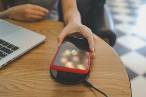 Charging mobile phone battery with wireless device in the table. Smartphone charging on a charging pad. Mobile phone near wireless charger. photo