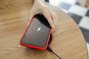 Charging mobile phone battery with wireless device in the table. Smartphone charging on a charging pad. Mobile phone near wireless charger. photo