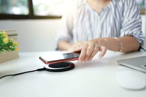 Charging mobile phone battery with wireless charging device in the table. Smartphone charging on a charging pad photo