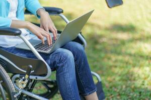 joven asiático mujer en silla de ruedas trabajando con ordenador portátil foto