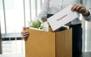 Business woman sending resignation letter and packing Stuff Resign Depress or carrying business cardboard box by desk in office. Change of job or fired from company. photo