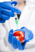 a person in blue gloves holding a tomato with a syringe photo