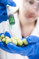 a person in blue gloves holding a tomato with a syringe photo