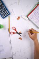 a person is writing on paper with a calculator, pencils, and other items photo