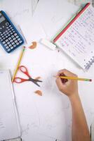 a person is writing on paper with a calculator, pencils, and other items photo