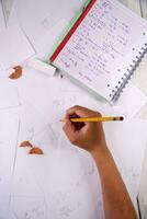 a person is writing on paper with a calculator, pencils, and other items photo