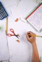 a person is writing on paper with a calculator, pencils, and other items photo