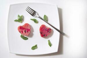 a white plate with a heart shaped piece of watermelon and a fork photo