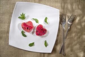 a white plate with a heart shaped piece of watermelon and a fork photo