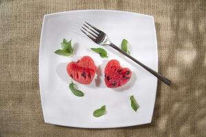 a white plate with a heart shaped piece of watermelon and a fork photo