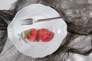 a white plate with a heart shaped piece of watermelon and a fork photo