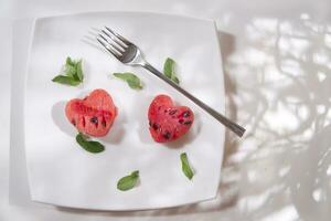 a white plate with a heart shaped piece of watermelon and a fork photo
