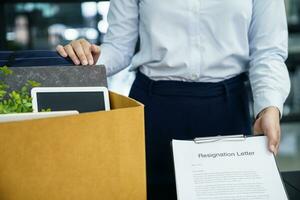 Business woman sending resignation letter to boss and Holding Stuff Resign Depress or carrying cardboard box by desk in office photo