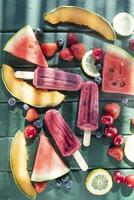 Popsicle made from red fruit on varied fruit table photo