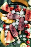 Popsicle made from red fruit on varied fruit table photo