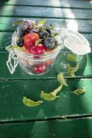 Colorful mixed fruit salad in glass container in green background. photo