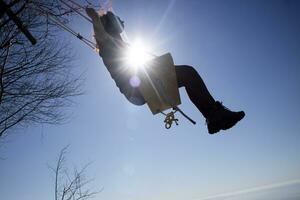 Girl shot against the light while having fun on the swing photo