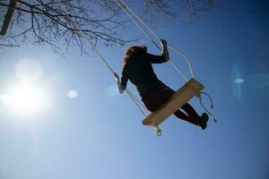 Girl shot against the light while having fun on the swing photo