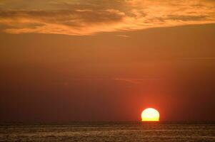 the sun sets over the ocean in a cloudy sky photo