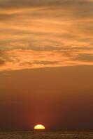 the sun sets over the ocean in a cloudy sky photo