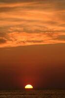 the sun sets over the ocean in a cloudy sky photo