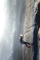 un persona en un cuerda alpinismo arriba un cascada foto