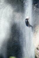 un persona en un cuerda alpinismo arriba un cascada foto