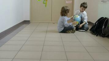twee kinderen zittend Aan de verdieping in de buurt een deur spelen met een wereldbol video