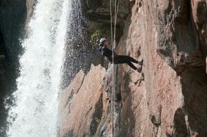 un persona en un cuerda alpinismo arriba un cascada foto