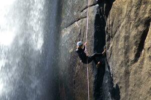 un persona en un cuerda alpinismo arriba un cascada foto