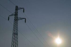 a silhouette of an electricity tower with the sun behind it photo