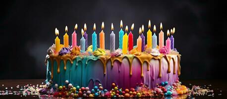 Rainbow birthday cake adorned with candles in various colors and decorative icing dripping down photo