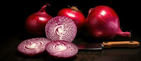 A photograph of red onions, both whole and sliced, along with a knife, set against a black background. photo