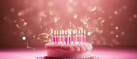 A pink birthday cake adorned with numerous pink candles and sparklers against a pink backdrop, photo