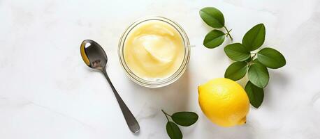 A jar of homemade lemon curd with a white spoon on top, seen from above, is photographed on photo