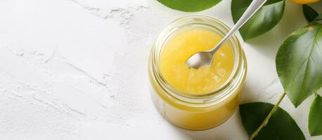 A jar of homemade lemon curd with a white spoon on top, seen from above, is photographed on photo