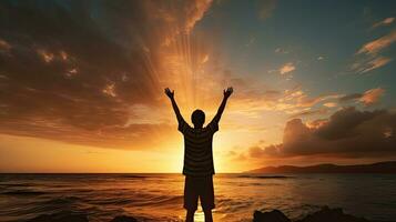 Boy s silhouette in sunset over sea representing religion worship prayer and praise photo