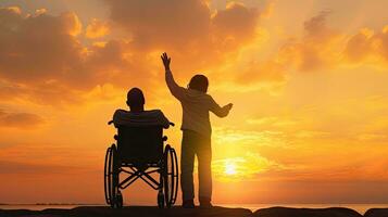 joven hombre en un silla de ruedas elevado manos con cuidador a puesta de sol foto