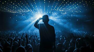 Singer performing on stage in packed stadium with bright lights and fans holding up phones photo