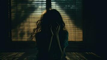 A girl her face hidden seated near a window casting a shadow photo