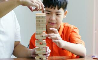 Asian father and son playing wood blocks game Carefree kid playing wood blocks game building constructor from blocks with father at home photo